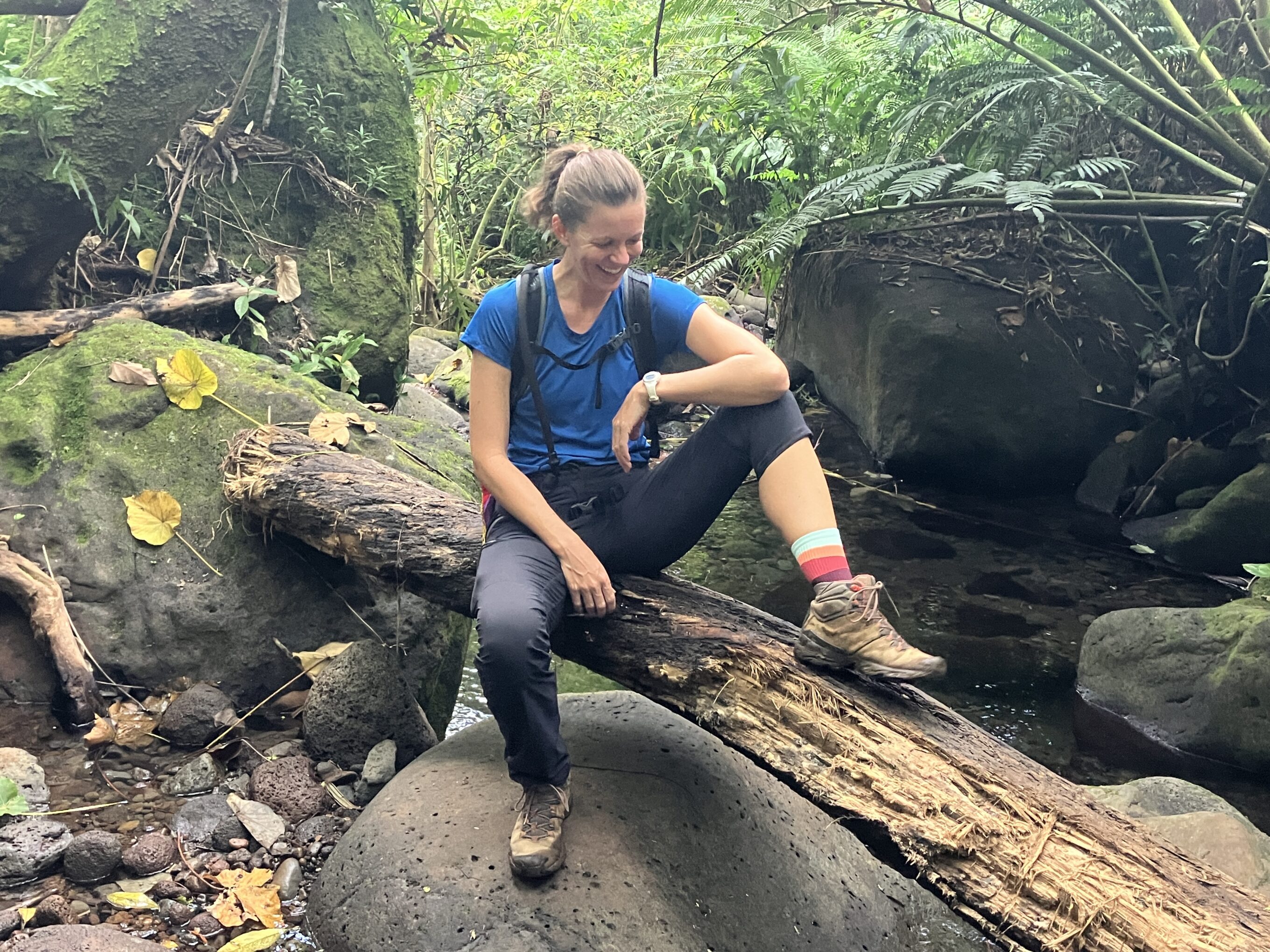 a woman sitting on a log in the forest wearing hiking socks