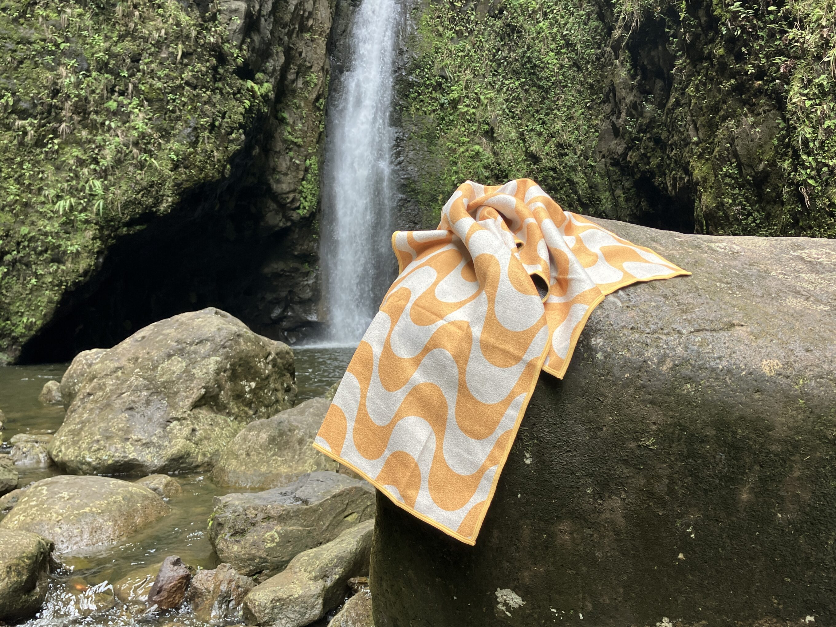 nomadix beach towel on a rock in front of a waterfall