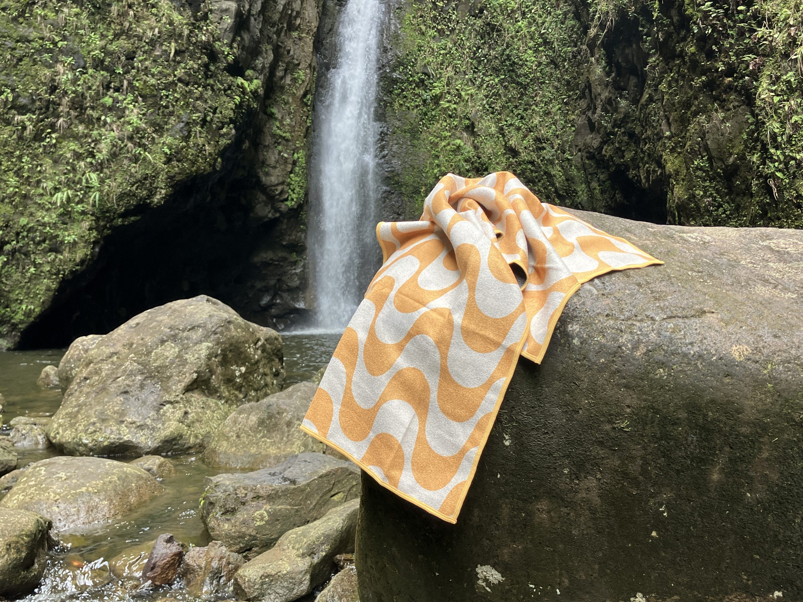 nomadix beach towel on a rock in front of a waterfall 