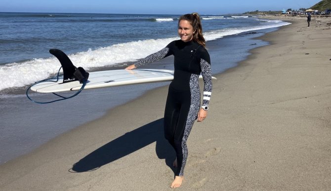 a woman wearing a hurley wetsuit walking on the beach with a surfboard
