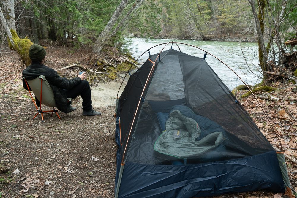a camper sitting in the REI flexlite chair by the river