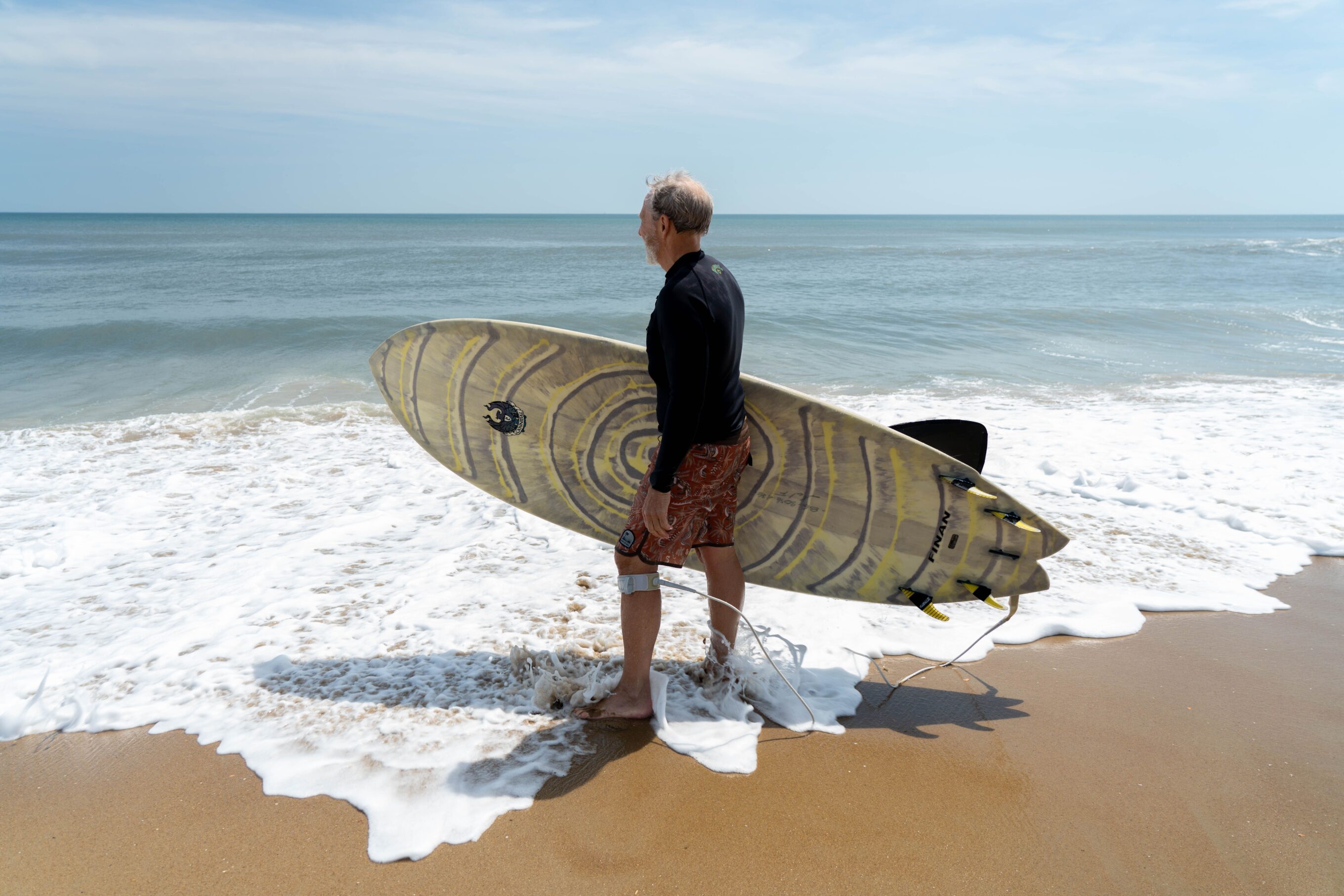 a man carries walks on the shore with a surfboard leash attached to his board