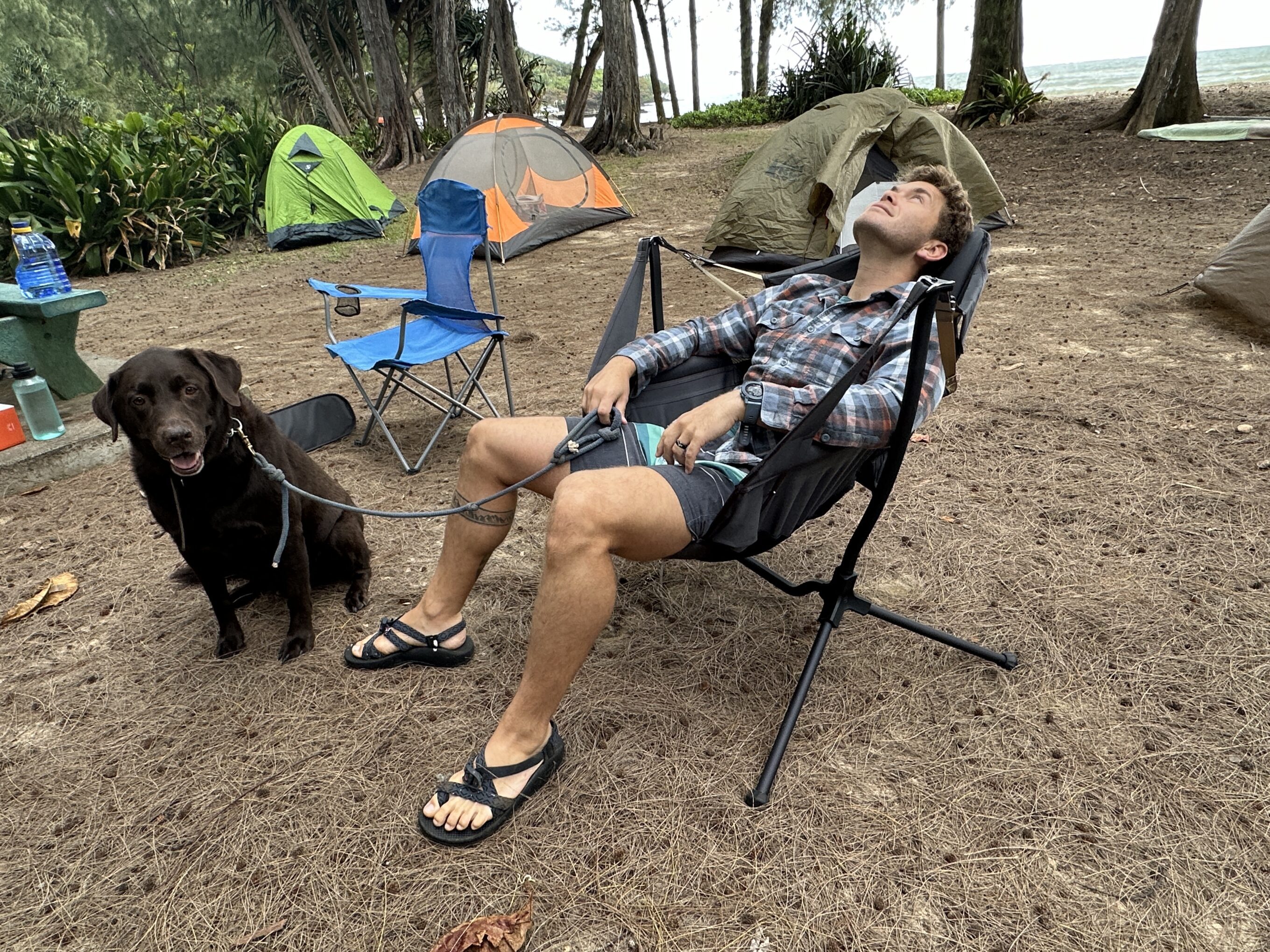 a man sitting in a camping chair with his dog next to him