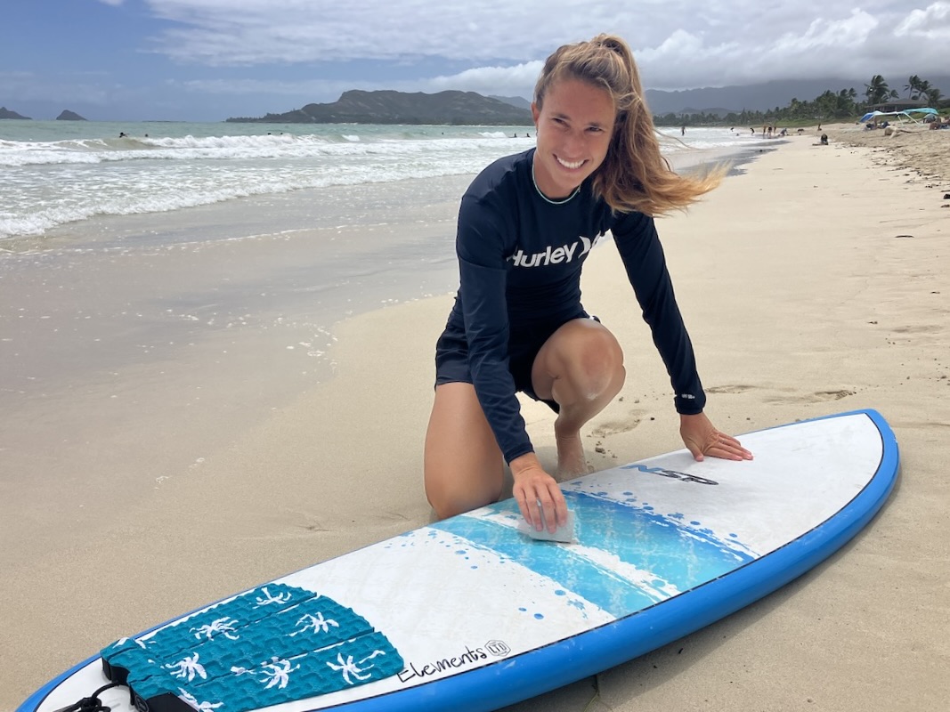 a woman wearing a rash guard waxing a surfboard