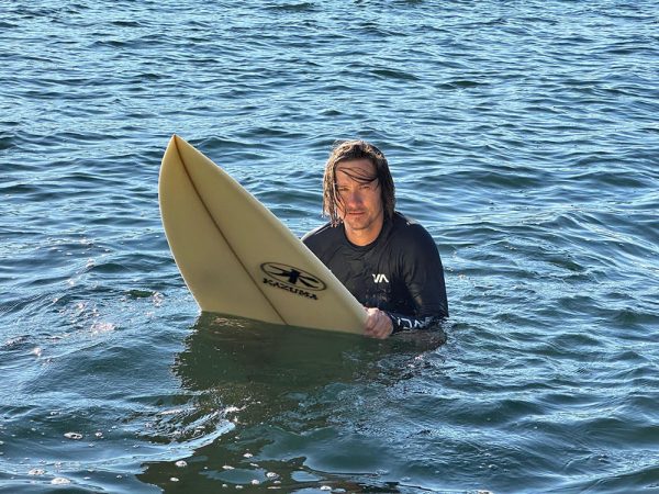 a surfer wearing a rash guard waits in the water for a wave