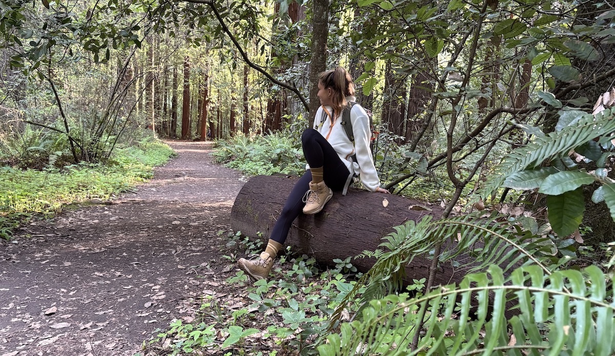 a woman sitting on a log wearing hoka kaha hiking boots