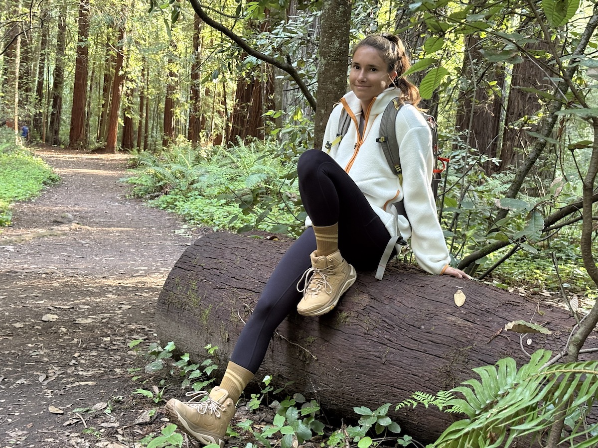 a woman sitting on a log in the forest wearing hiking boots