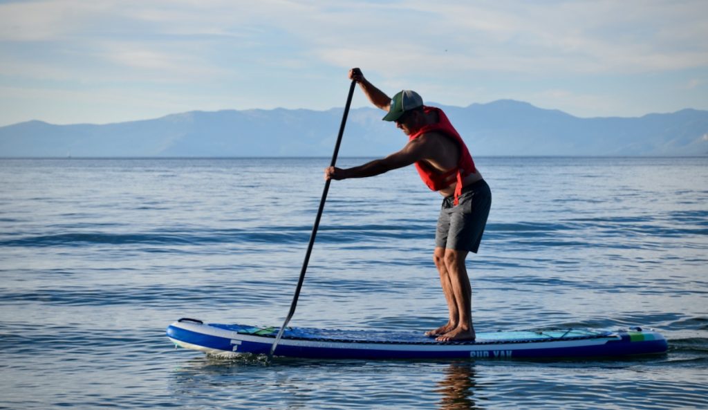 A man paddling an inflatable paddle board at dusk on Lake Tahoe