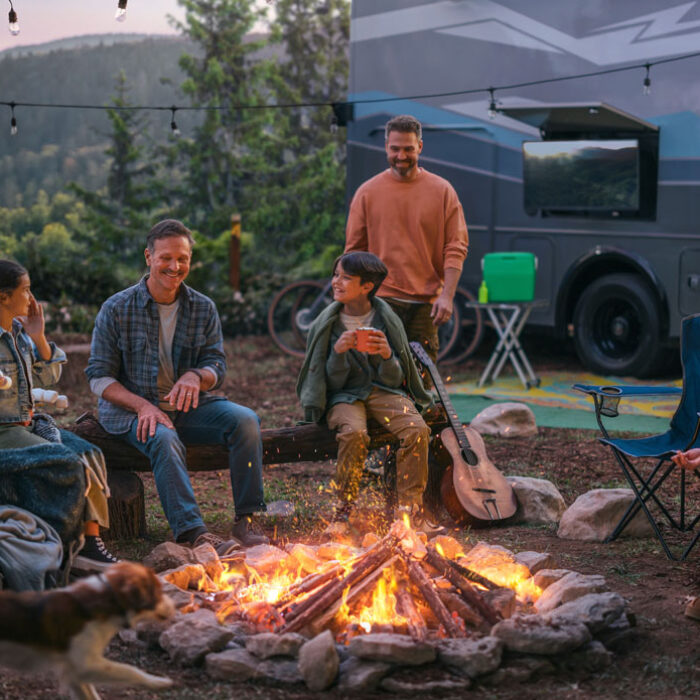 A family sits around a campfire next to their RV in the evening