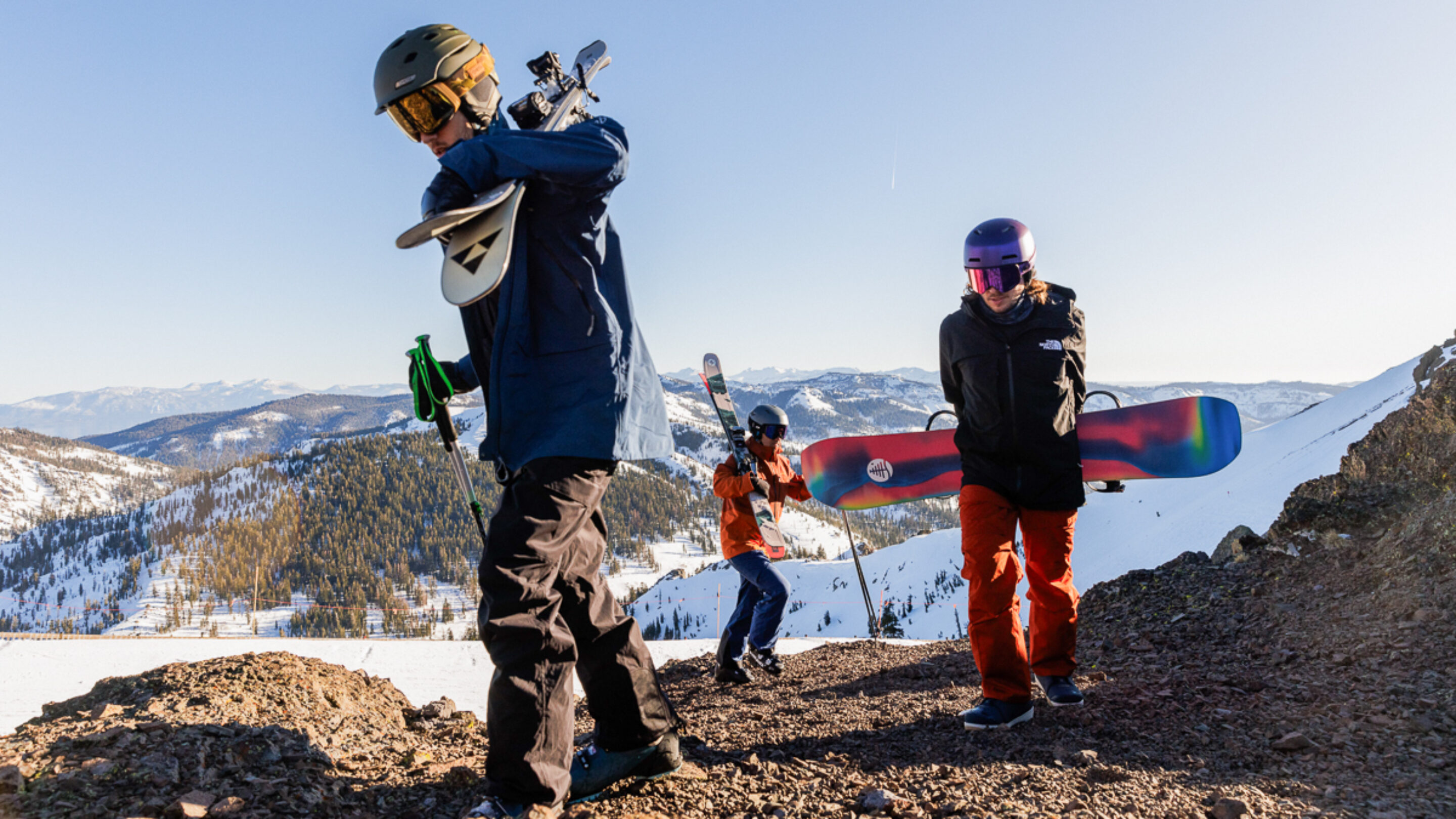 three men hiking up mountain with snowboard and ski gear