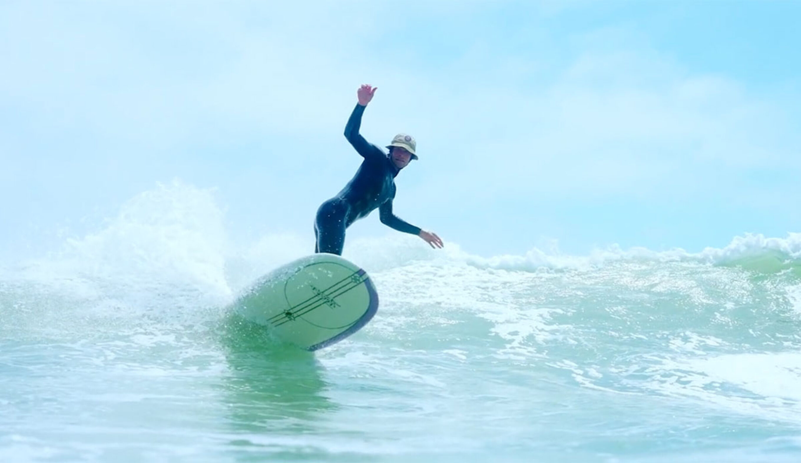 A man surfing with a surf helmet/bucket hat