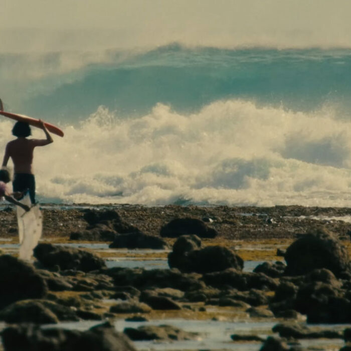 Craig Anderson with surfboard walking towards a wave for Samudra Spirit Glitters.