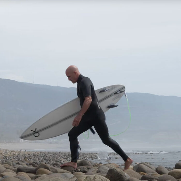 Kelly Slater walking on rocks with a surfboard