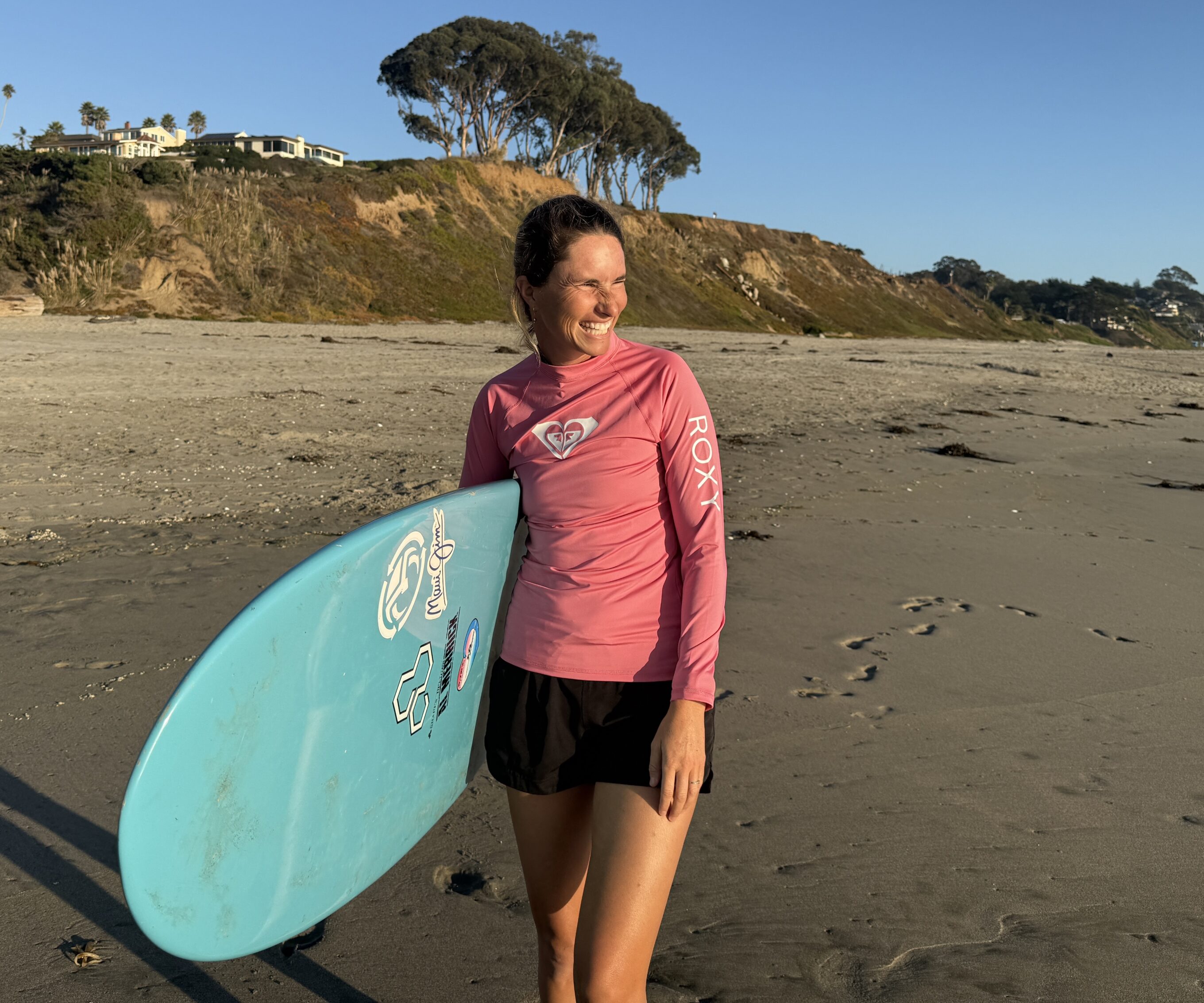a woman holding a surfboard and wearing a roxy rash guard 