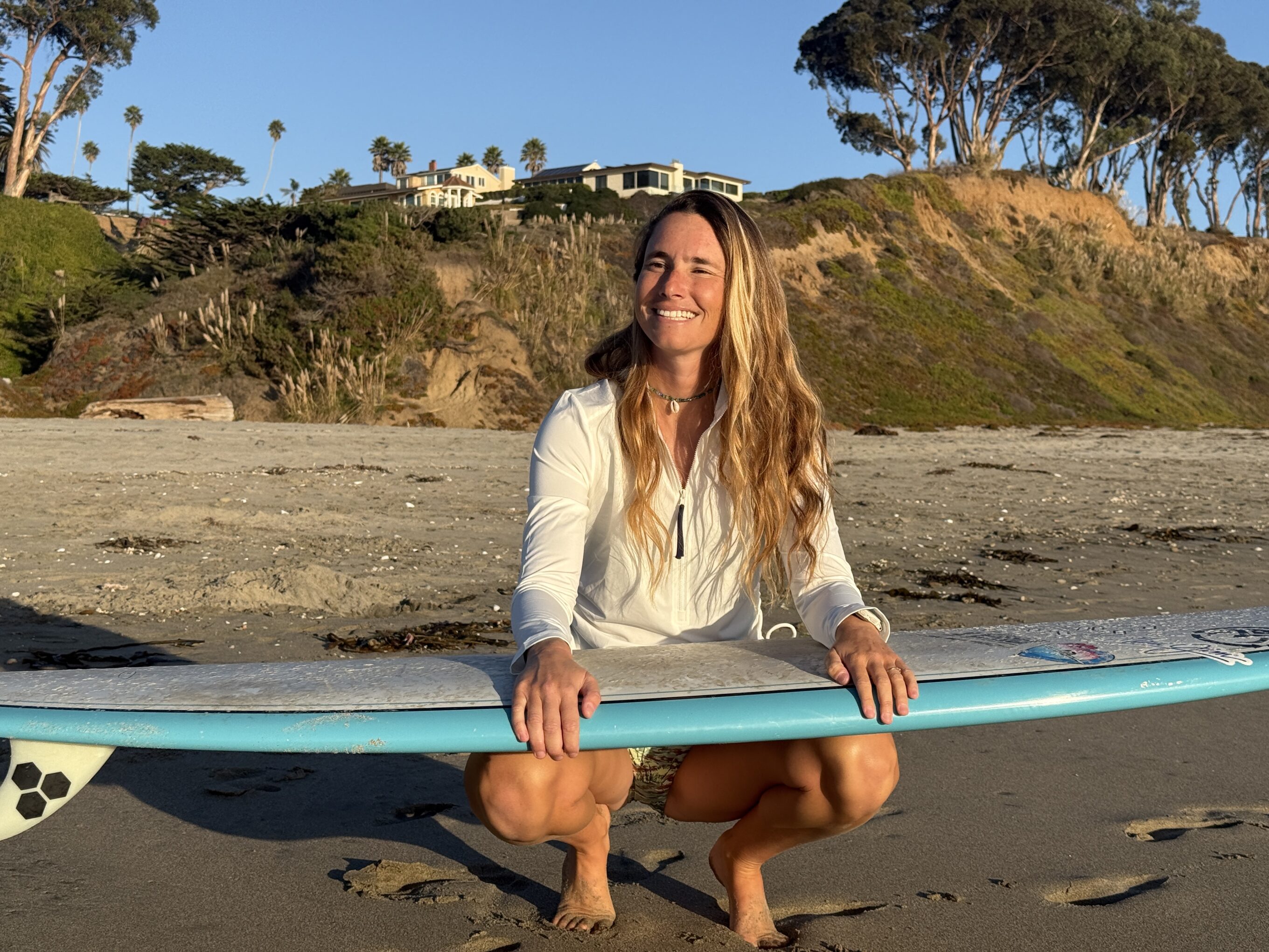 a woman holding a surfboard and wearing a white rash guard 
