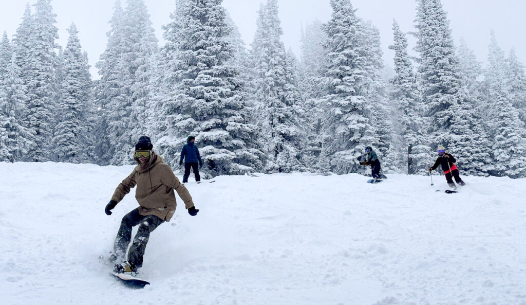 4 women skiing and snowboarding in powder