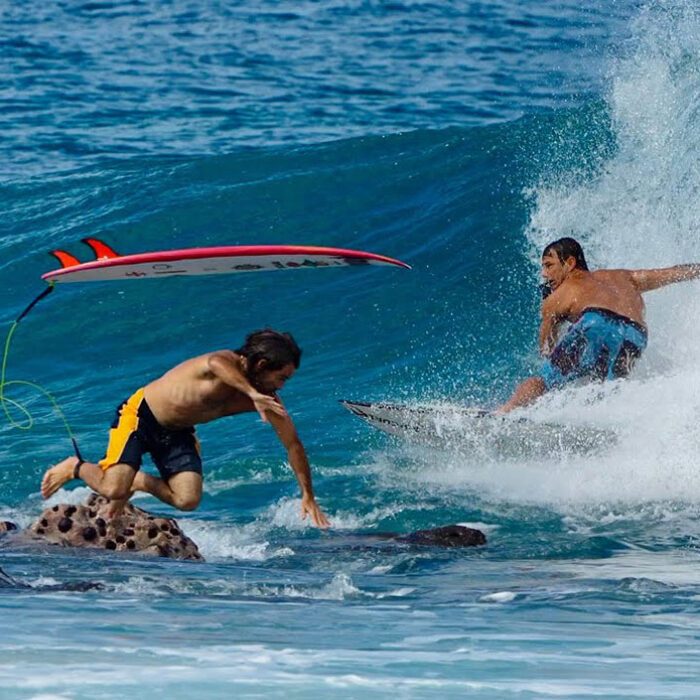 Mason Ho jumping off a rock as Sheldon Paishon surfs past him