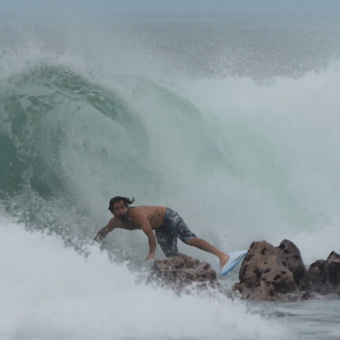Mason Ho surfing in front of rocks